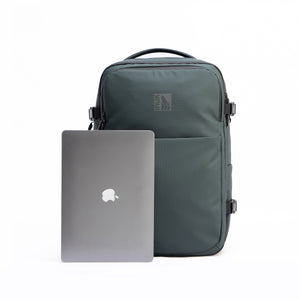 INUK NAVI Black Forest Green backpack beside a laptop, showing its 16-inch laptop capacity