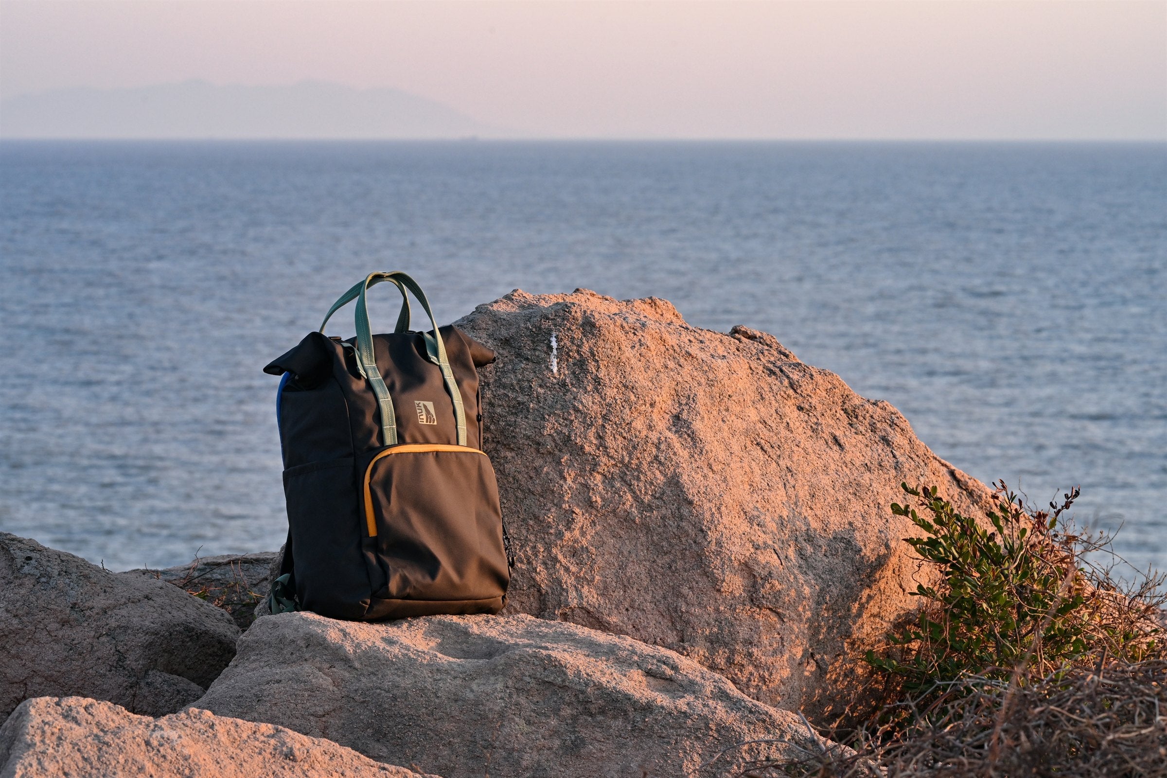 Black and olive INUK WANDER backpack on coastal rocks above the water